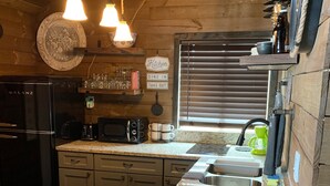 A kitchen with granite countertops, a refrigerator, a microwave, a sink, and wooden cabinets. There are two hanging light fixtures and a window with blinds. - ❤️Dixieland Delight❤️Studio. Pet friendly WITH FEE 🐕🐈❤️❤️❤️❤️❤️ (New Port Richey)
