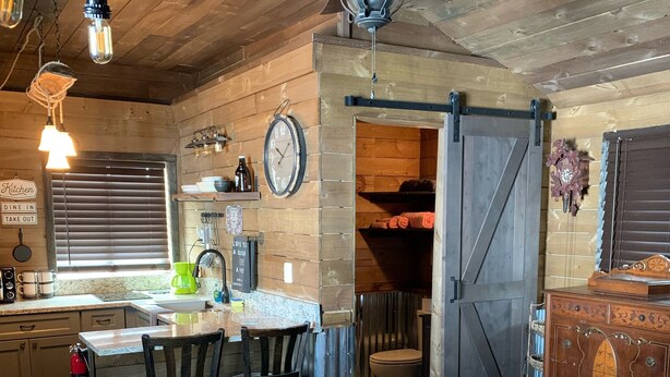 A rustic kitchen with wooden walls, a large clock, and a dining area with a bar stool and chairs. - ❤️Dixieland Delight❤️Studio. Pet friendly WITH FEE 🐕🐈❤️❤️❤️❤️❤️ (New Port Richey)