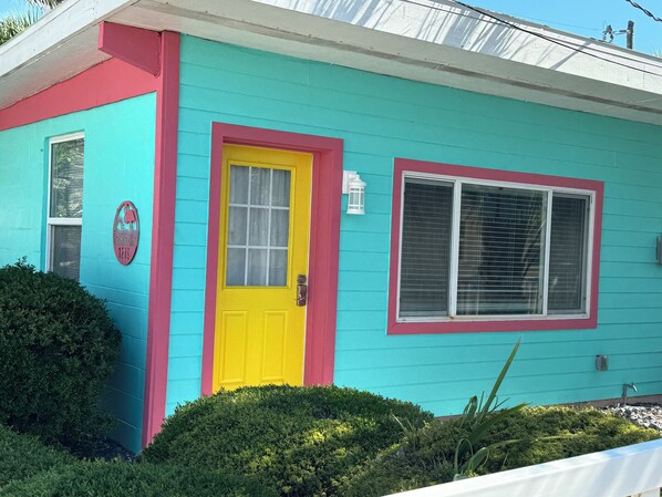 A house with a bright yellow door, a window with blinds, and a mailbox.