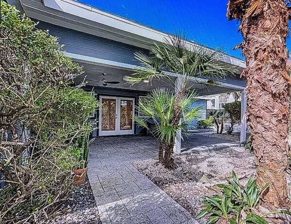 A modern building with a paved entrance, palm trees, and a stone pathway.