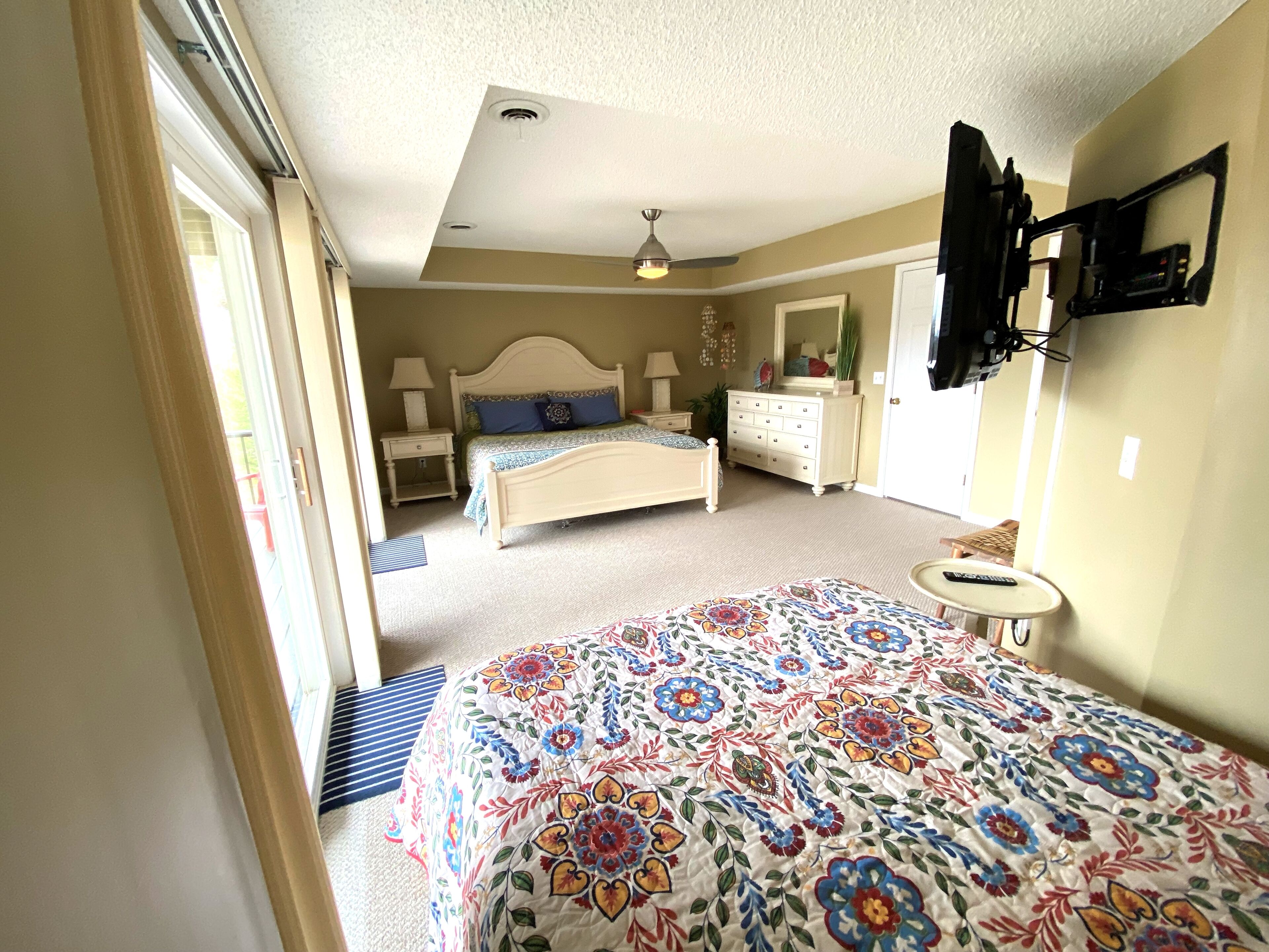 A bedroom with a bed, a dresser, a nightstand, a mirror, and a television mounted on the wall.