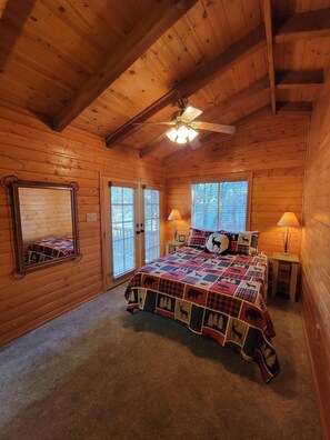 A cozy log cabin bedroom with a large bed, two bedside lamps, a ceiling fan, and a mirror. - Cozy Two Bedroom Cabin with Fireplace! (Lakeside)