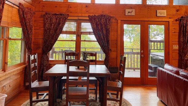 Interior de una cabaña de madera con una mesa de comedor, sillas y un sofá.