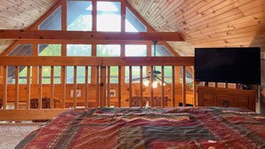Una habitación de cabaña acogedora con una cama grande, vigas de madera en el techo y un televisor sobre un aparador de madera.