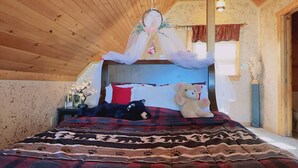 Un dormitorio acogedor con techo de madera, una cama con manta escocesa roja y negra, un osito de peluche y un dosel decorativo.