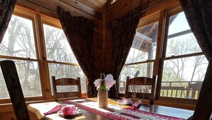 Comedor de una cabaña de madera con una mesa preparada para cuatro personas, rodeado de sillas.