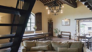 A cozy living room with a sofa, wooden beams, a chandelier, and a dining area. - Villa Betta By MMega (Città di Castello)