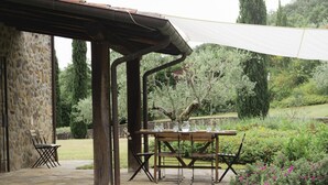 An outdoor patio with a stone wall, a wooden table, and chairs. - Villa Betta By MMega (Città di Castello)