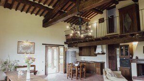 A spacious kitchen with wooden beams, a dining area with a table and chairs, and a balcony with a railing. - Villa Betta By MMega (Città di Castello)