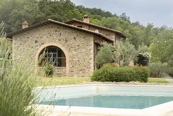 A stone building with a pool, surrounded by greenery.