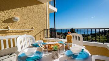 A balcony with a table set for two, featuring a clear view of the sea and a mountainous landscape.