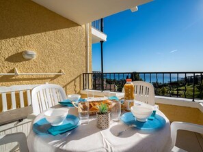 A balcony with a table set for two, featuring a clear view of the sea and a mountainous landscape.