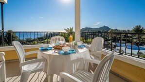 A balcony with a table set for breakfast, overlooking a scenic view of the sea and hills. - Le Village (C4221) by Interhome (Agay Village Cap Esterel)