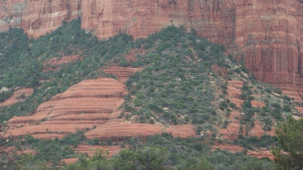 Un paysage montagneux accidenté, caractérisé par des formations rocheuses rouges en strates et une végétation verte clairsemée.