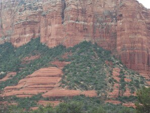Paisagem montanhosa acidentada com formações rochosas vermelhas em camadas e vegetação verde esparsa.