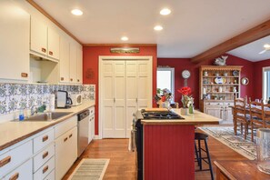 A kitchen with white cabinets, a red accent wall, a dining area with wooden chairs, and a clock on the wall.
