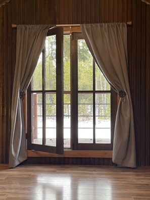 A room with a large window, wooden floor, and curtains.
