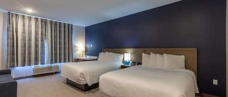 Una habitación de hotel con dos camas, un escritorio, una silla y una ventana con cortinas.