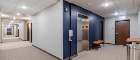 A hallway with an elevator, a bench, and a trash can.