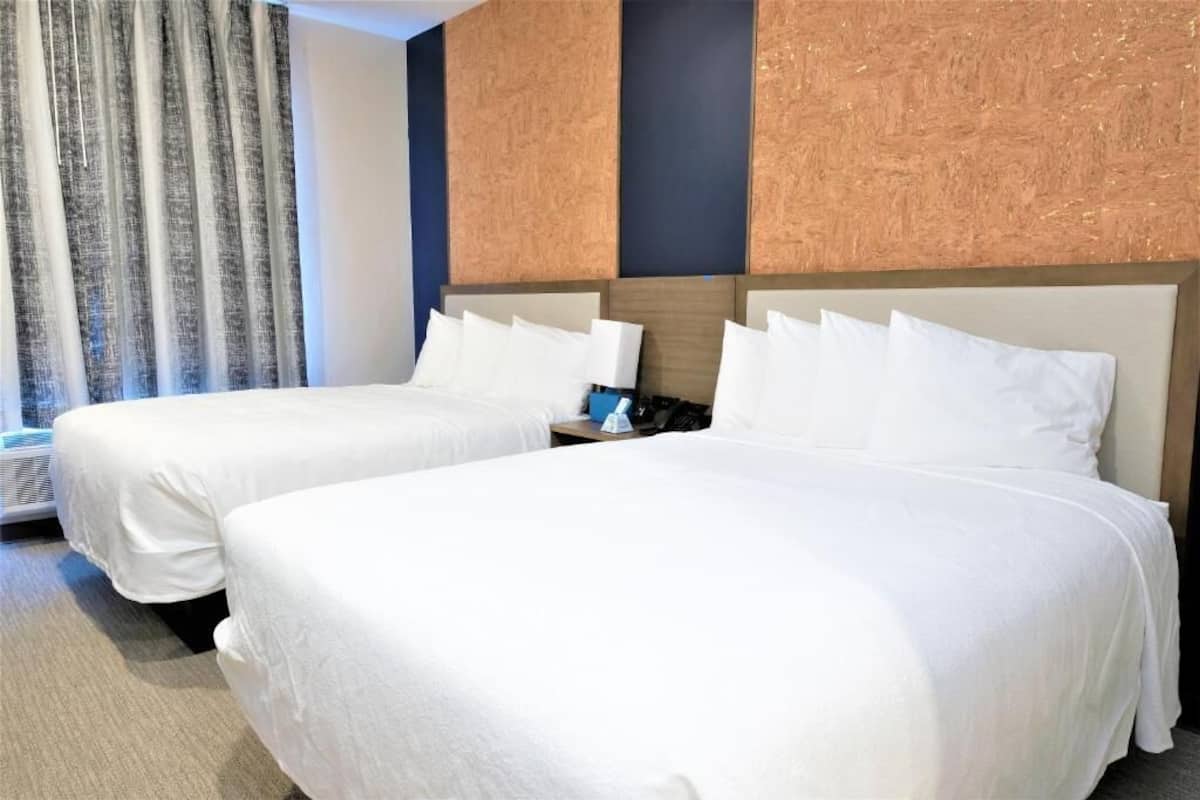 A hotel room with two beds, a nightstand, and a wall-mounted air conditioning unit.