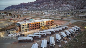 Um hotel moderno com vários edifícios, estacionamento e montanhas ao fundo.