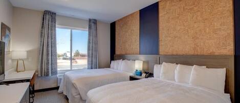 A hotel room with two beds, a desk, a chair, a window with curtains, and a view of the outside.