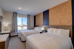 Habitación de hotel con dos camas, un escritorio, una silla, una ventana con cortinas y vistas al exterior.