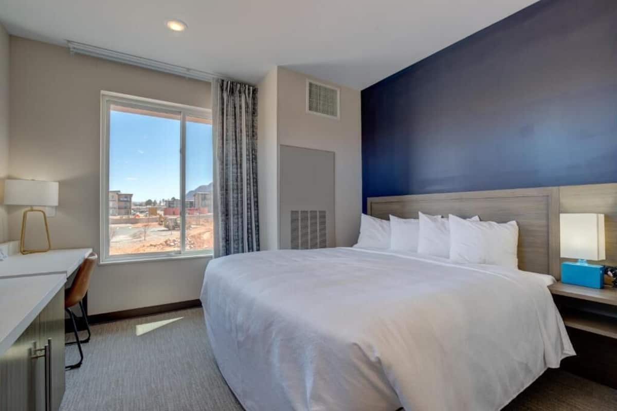 A hotel room with a large bed, a desk, and a window with a view of the outside.