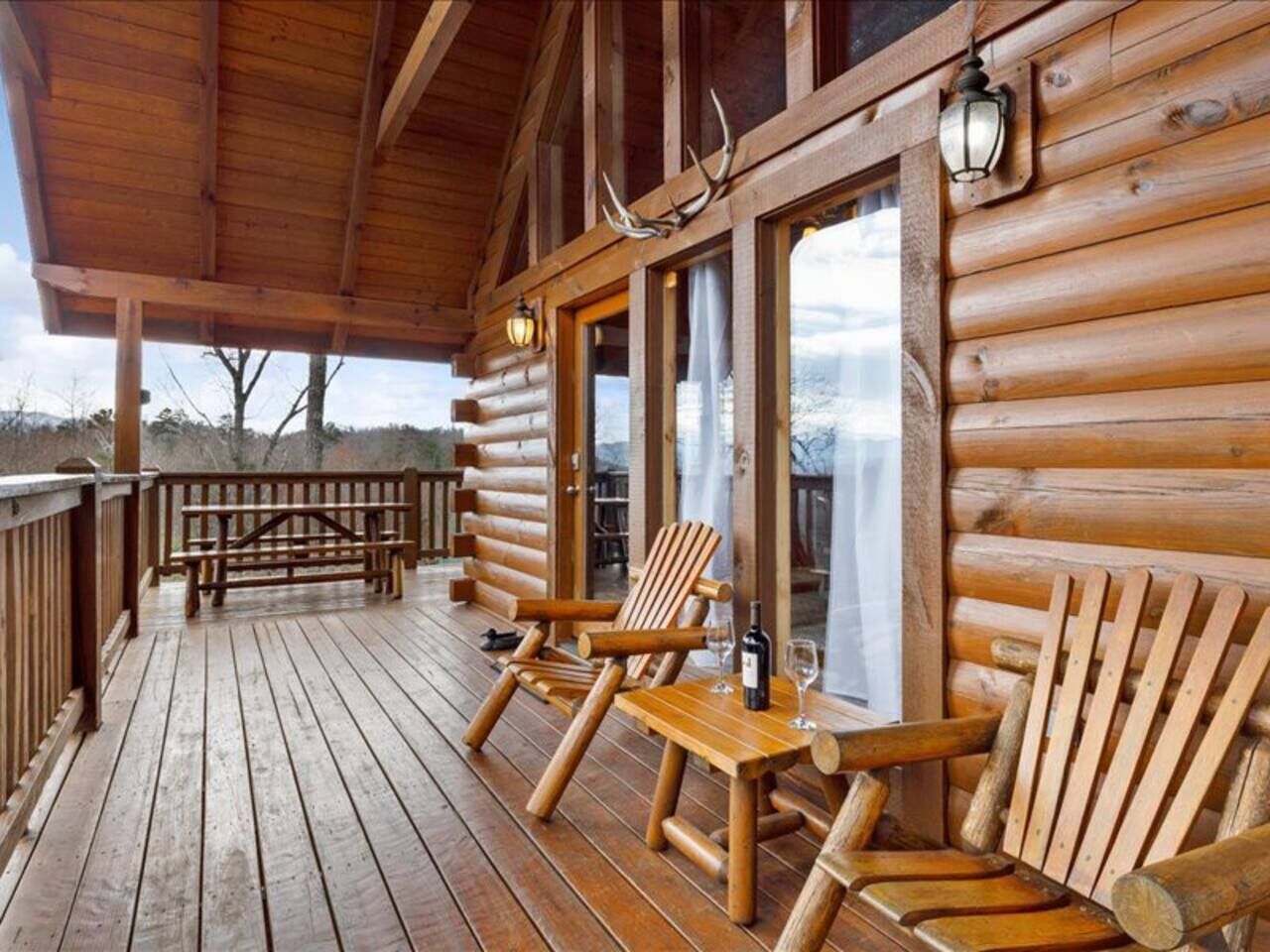 A wooden deck with Adirondack chairs and a table, overlooking a snowy landscape.