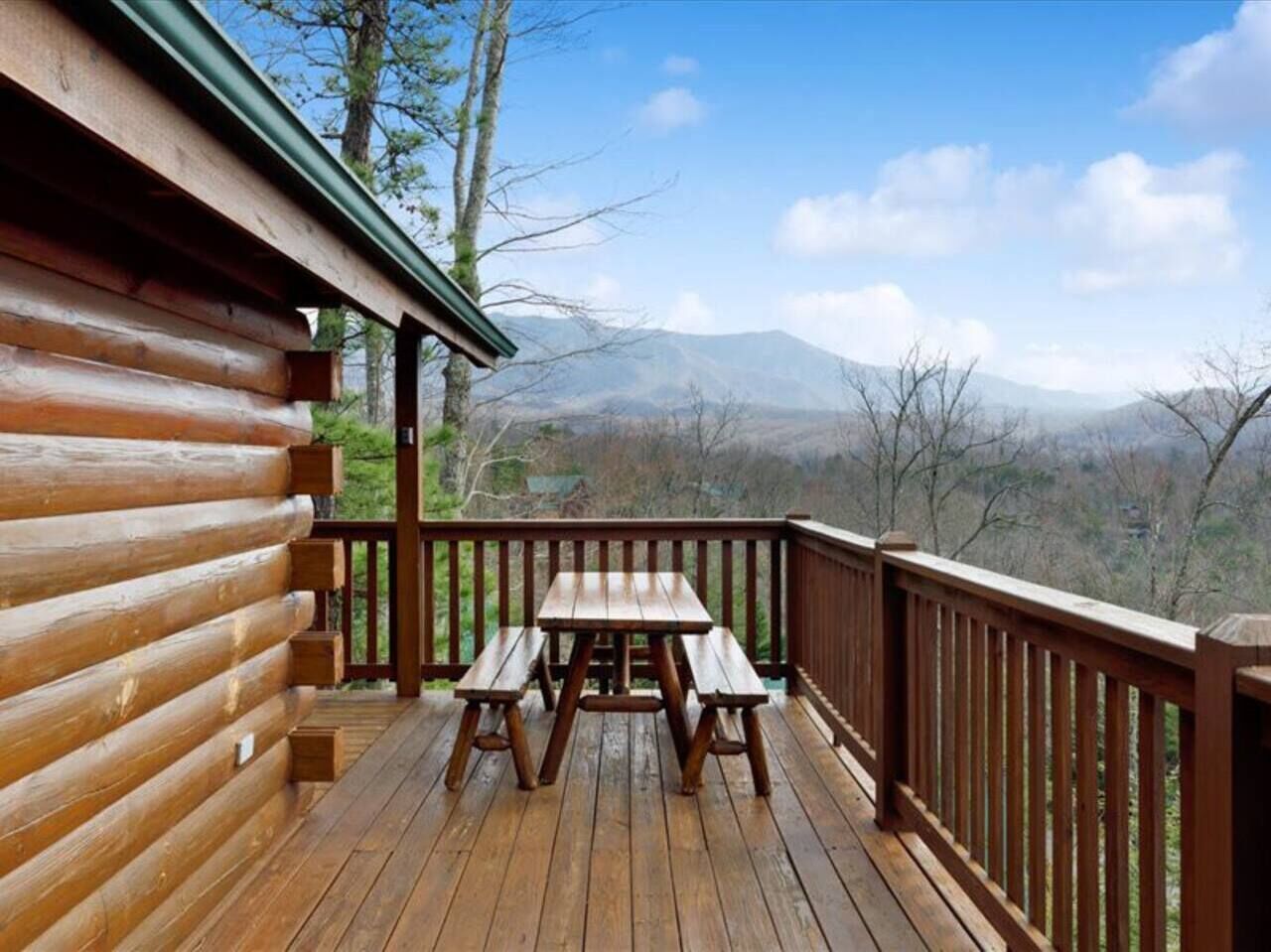 A wooden deck with a picnic table and benches, overlooking a mountainous landscape.