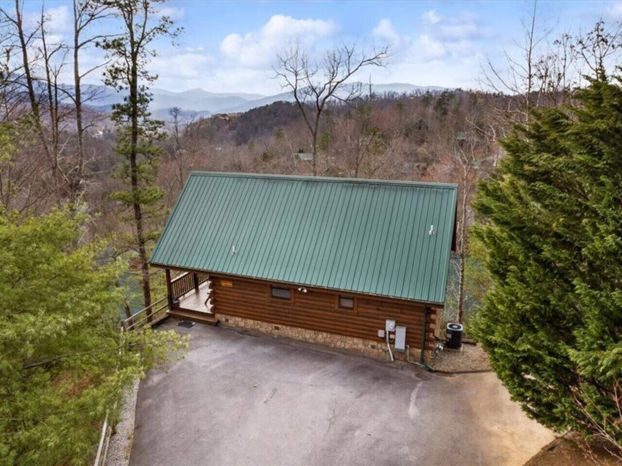 A cabin with a green roof, surrounded by trees and a mountainous backdrop.