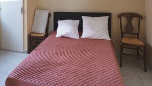 Uma cama com colcha rosa, duas almofadas brancas e cabeceira de madeira.
