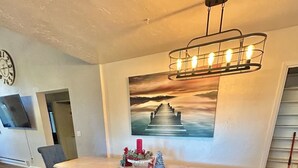 A modern living room with a wooden bench, a TV mounted on the wall, and a painting of a sunset. - Cozy Family Friendly Lodge, 2 Games Rooms, Hot Tub, EV Charger (Prescott)