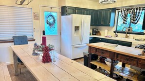 A kitchen with a wooden table, a refrigerator, and green cabinets. - Cozy Family Friendly Lodge, 2 Games Rooms, Hot Tub, EV Charger (Prescott)