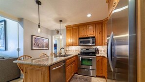 A kitchen with wooden cabinets, a stainless steel refrigerator, a built-in oven, and a granite countertop. - Chamonix 10: Charming, Walk to Canyon Lodge (Mammoth Lakes)