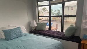 A bedroom with a bed, pillows, a window seat, and a view of the outside.