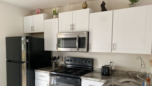 A modern kitchen with white cabinets, a black refrigerator, a microwave, a stove, and a sink.
