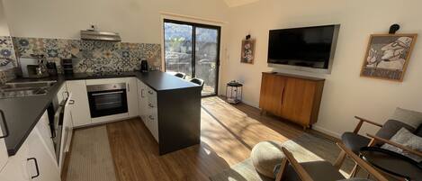 A modern kitchen with a large island, a dining area with a TV, and a living room with a sofa and chairs.