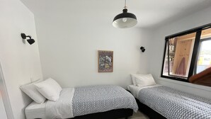 A small, modern bedroom with two single beds, a black chair, a patterned rug, a wall-mounted light, and a window with a view. - Derby Bank House Cabin- one bedroom with full kitchen. In the centre of town (Derby)