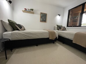 Un dormitorio con dos camas, un pequeño estante con adornos, un cuadro en la pared y una ventana con vistas.