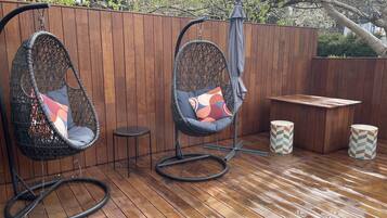 Twee hangstoelen met kussens, een klein rond tafeltje en een bank.