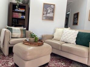 Una sala de estar con un sofá color beige, una mesa de centro con una planta, una estantería y un cuadro en la pared.