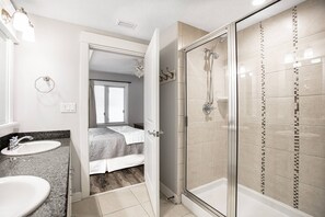 Een moderne badkamer met twee wastafels en een douche, met een bed in de aangrenzende kamer.