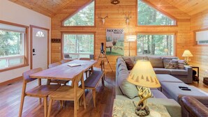 Interior de una cabaña con paredes de madera, una mesa de comedor, un sofá y un cartel con un ciervo.