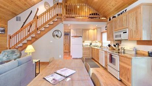 Amplia sala de estar con una escalera de madera, una mesa de comedor con una revista y una cocina con armarios y electrodomésticos de madera.