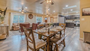 A spacious living room with a dining area, wooden furniture, ceiling fans, and a kitchen in the background.