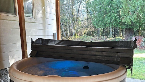 A hot tub under a wooden pergola with steps leading up to it, surrounded by a garden and trees. - Little Woods Outpost | Wifi, AC, Hot tub (Randle)