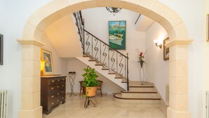 A grand staircase with a wrought iron railing, a potted plant, and a framed painting on the wall.