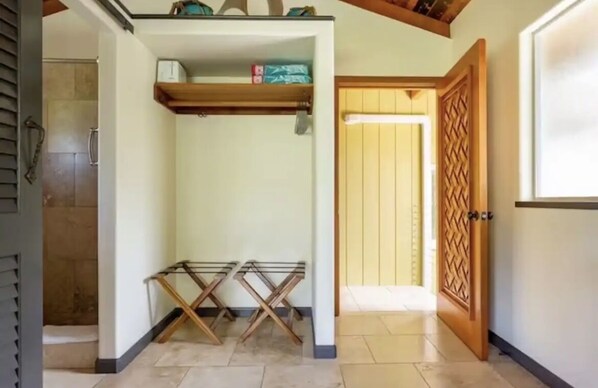A room with a wooden door, a tiled floor, and a shelf with boxes.