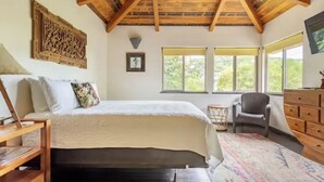 A bedroom with a wooden ceiling, a bed, a chair, a dresser, and a window with a view of greenery. - Escape to your private oasis (Hilo)